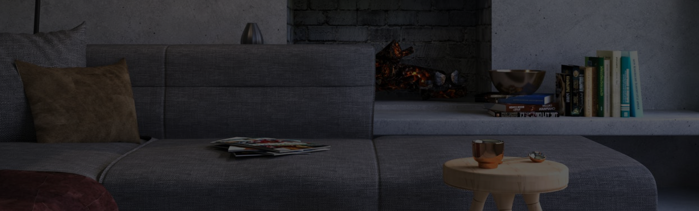 Dark decorative interior image showing a grey sectional sofa, a small round table, books and a lit fireplace.